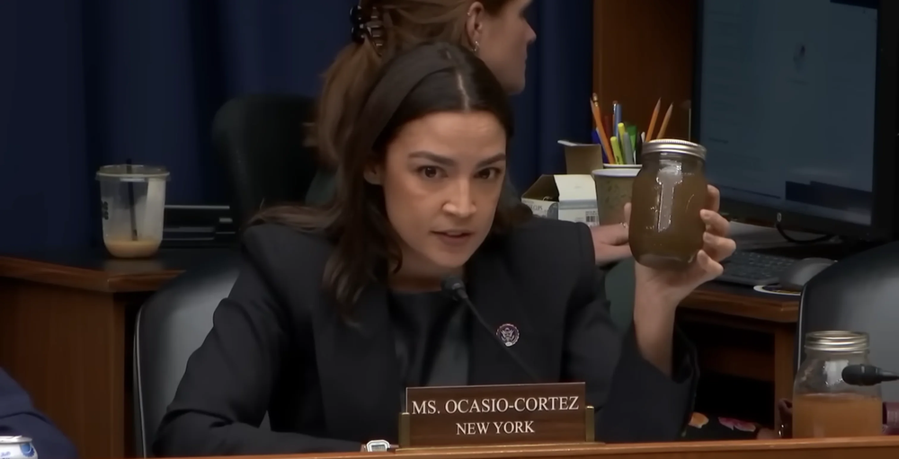 Representative Alexandria Ocasio-Cortez holds up a jar of discoloured water at a congressional hearing